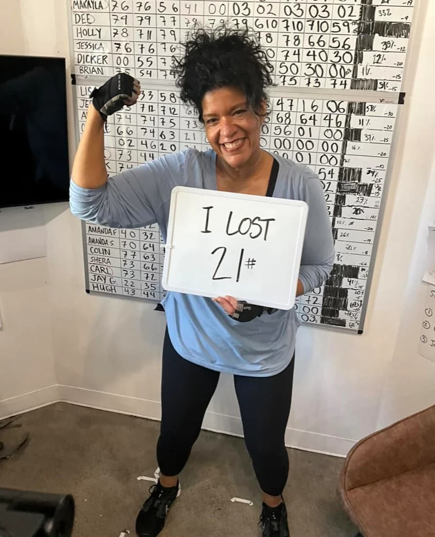 Leaner Fitness member holding a sign reading I lost 21 lbs